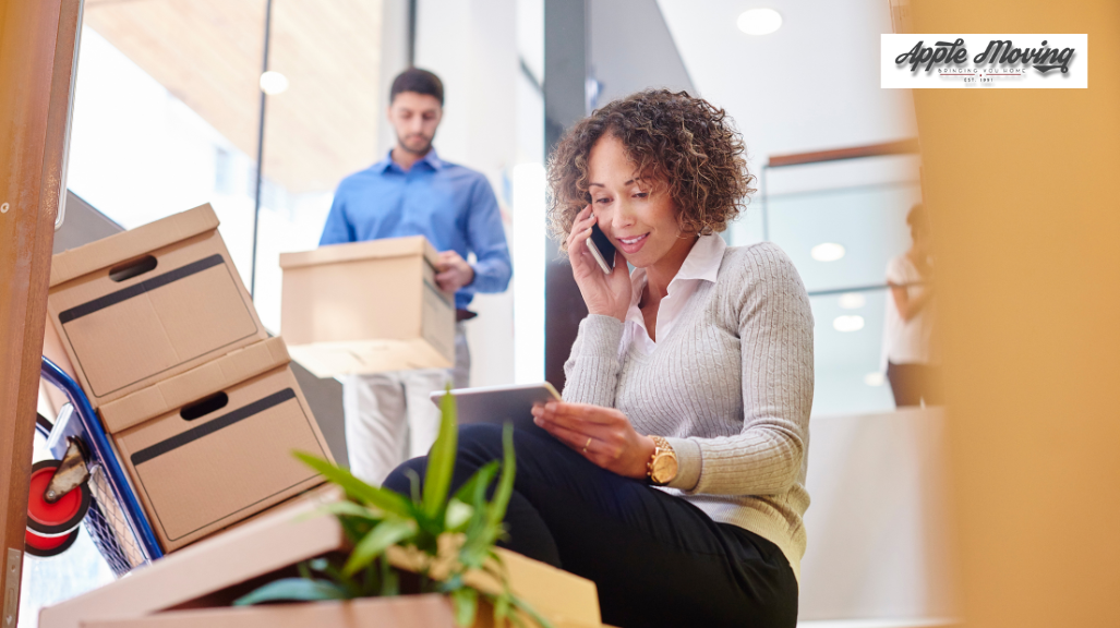 man lifting box standing behind woman holding phone